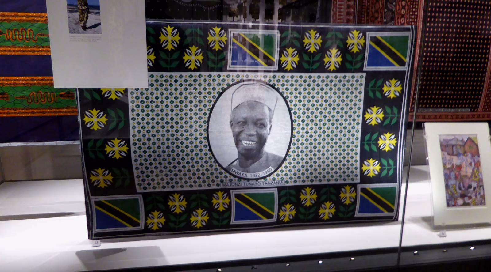 A kanga displayed flat, a printed portrait at its centre inside a wide patterned border.