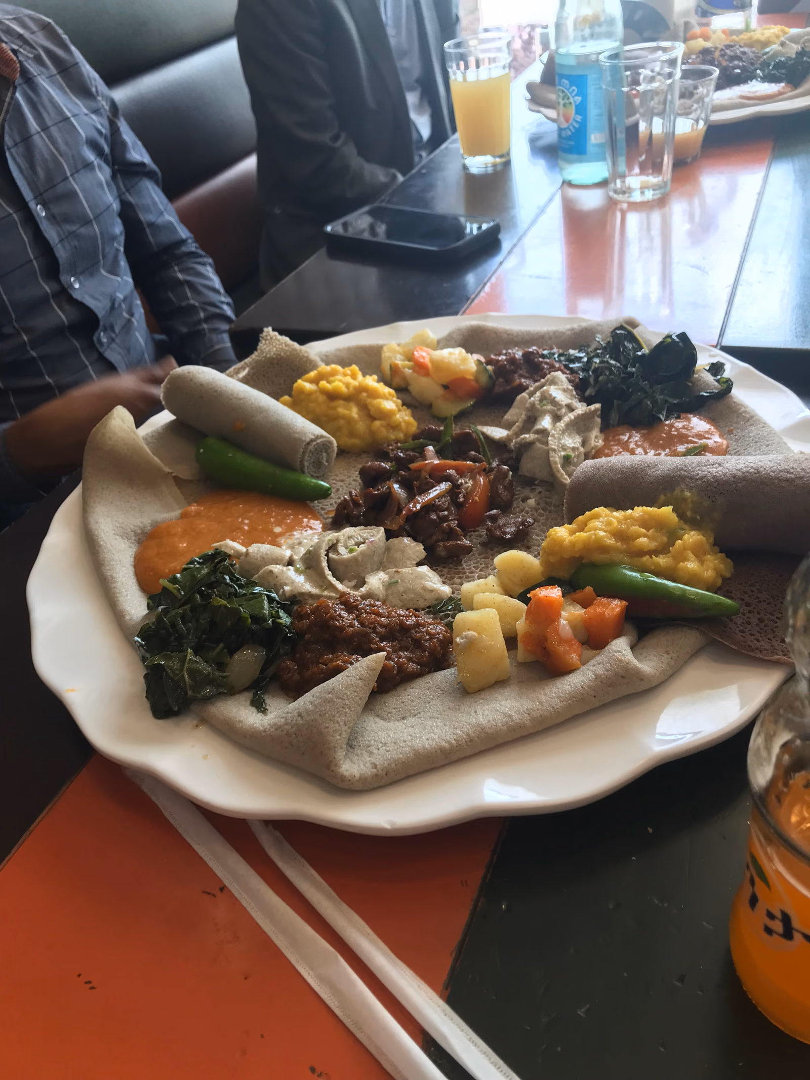 A wide platter lined with pale, spongy injera, topped with small mounds of lentil, green, tomato and vegetable stews, with rolled injera at the edge.